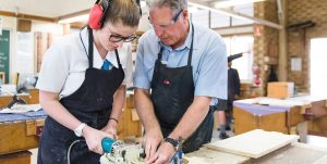 Vocational education and training. Male teacher showing female student woodwork